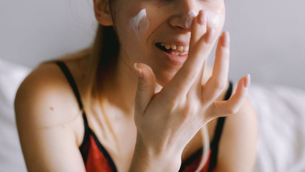 smiling woman applying cream on face