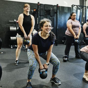 smiling woman doing kettlebell swings while working out during class in gym