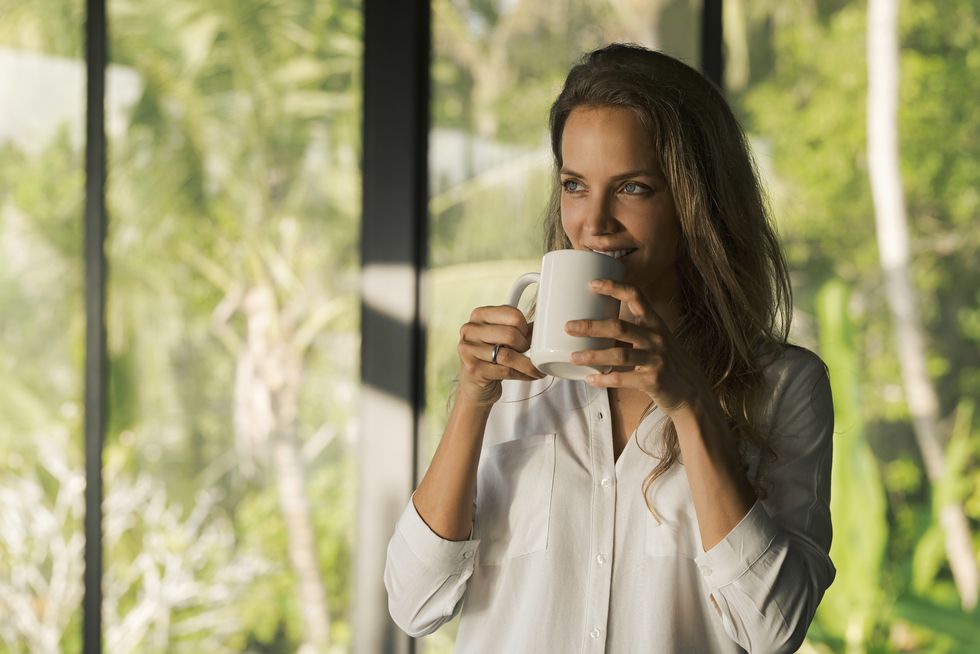 smiling woman drinking coffee at home in front of lush tropical garden