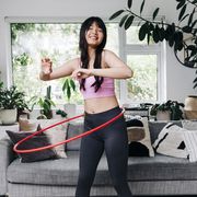 smiling woman exercising with plastic hoop in living room