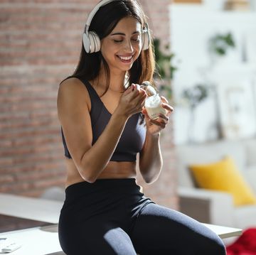 smiling woman listening music through headphones and having yogurt at home