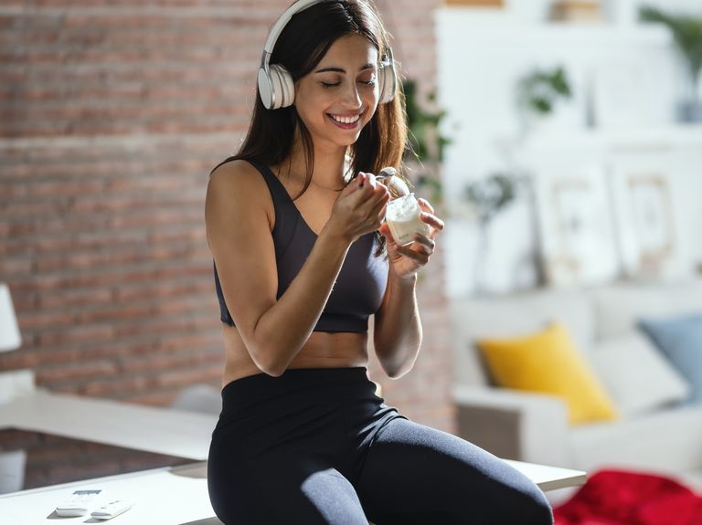 smiling woman listening music through headphones and having yogurt at home