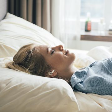 smiling woman lying in bed and listening to music through her wireless earphones