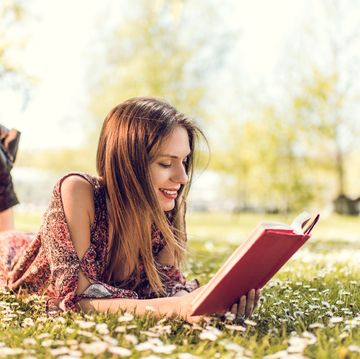 smiling woman relaxing in grass and reading a book