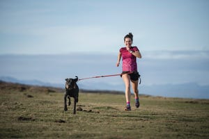 smiling woman running with dog on grass