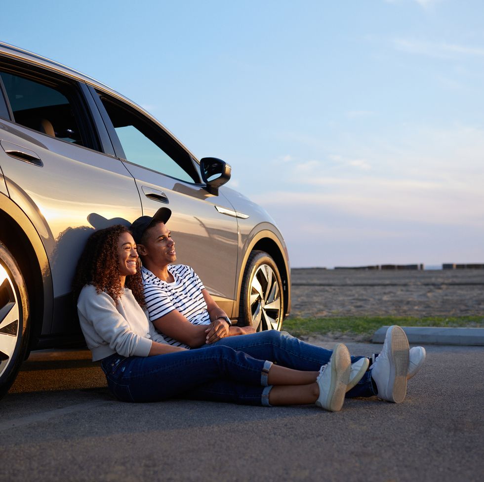smiling woman sitting with boyfriend against car during sunset