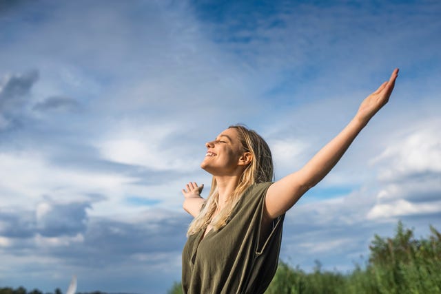 una mujer sonríe mientras abre los brazos mirando al cielo