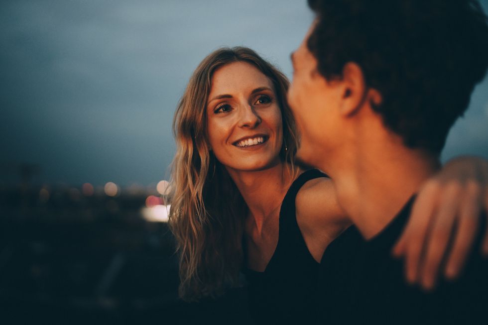 smiling woman with arm around looking at man while sitting on terrace at dusk