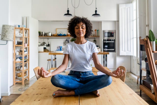 Smiling woman with closed eyes in yoga pose on table at home