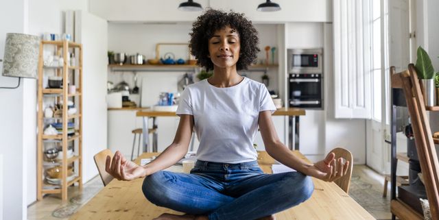 Smiling woman with closed eyes in yoga pose on table at home