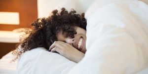 best bamboo sheets  a smiling woman with dark curly hair in bed under the covers, head on a white pillow