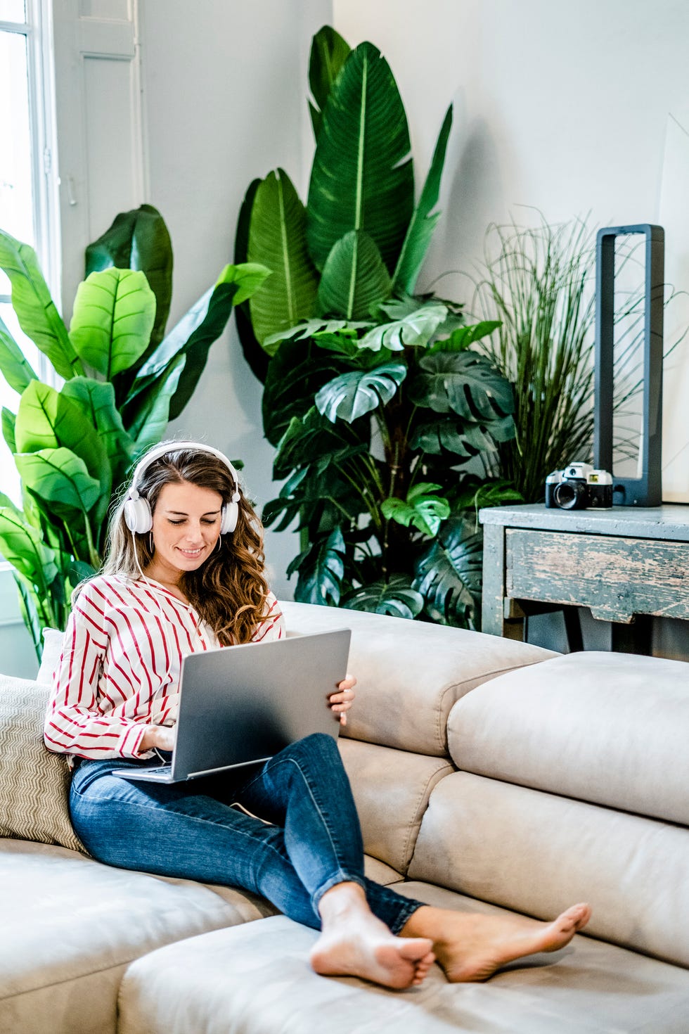 virtual happy hour ideas - Smiling woman with laptop and headphones sitting on couch