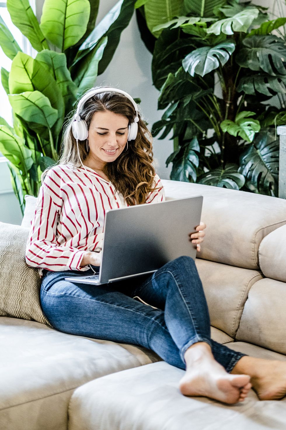 games to play on zoom - Smiling woman with laptop and headphones sitting on couch