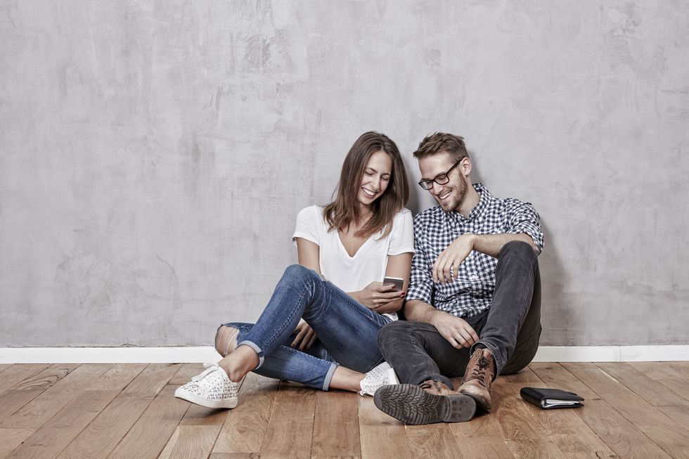Smiling young couple sitting on the floor with cell phone