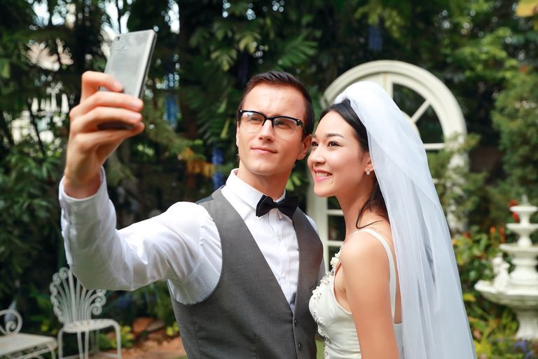 smiling young wedding couple taking selfie outdoors