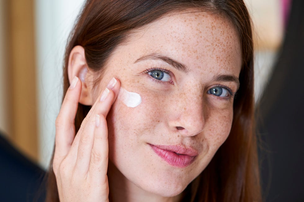 smiling young woman applying cream on her face