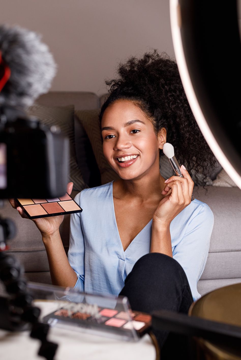 smiling young woman applying make up while being filmed in camera