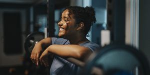 smiling young woman leaning on barbell at health club