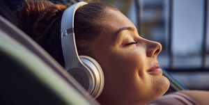 smiling young woman lying on hammock on balcony listening music with headphones