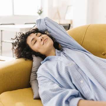 smiling young woman with eyes closed resting on sofa at home
