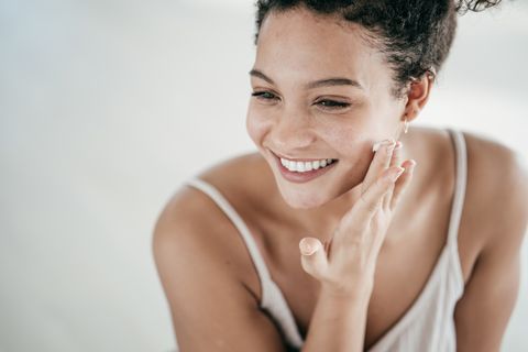 smiling young women applying moisturiser to her face