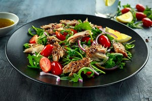 Smoked Mackerel Salad with tomato, chopped red onion, Ruccola on black plate.