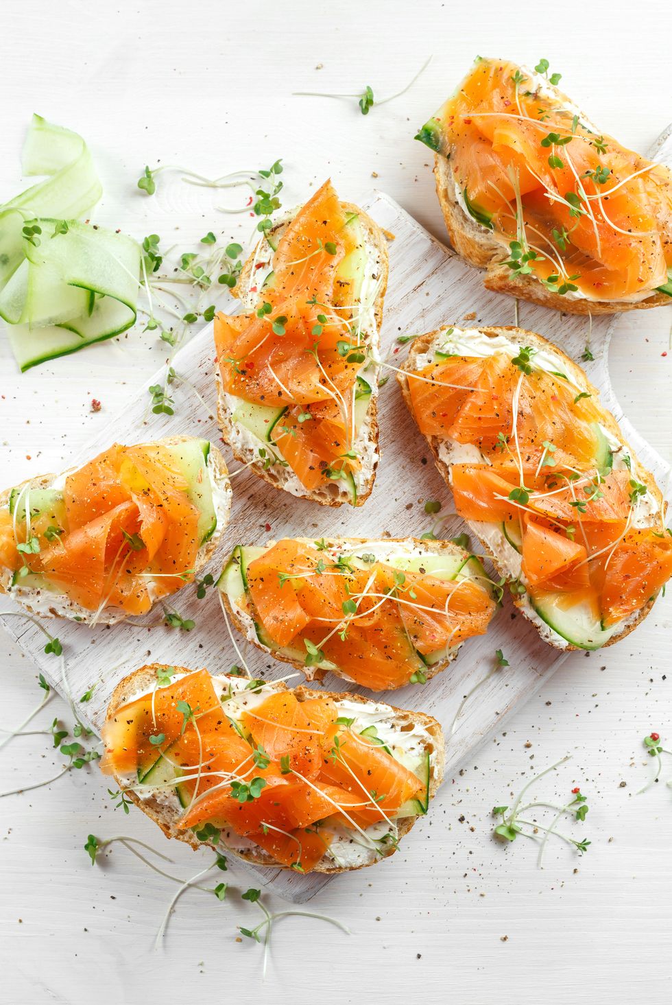 Smoked salmon bruschettas with soft cheese and cucumber shavings on white board.