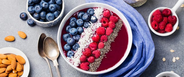 Smoothie bowl with fresh raspberry, blueberry, coconut flakes and chia seeds. Grey stone background. Top view.