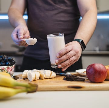 man preparing a protein drink in a kitchen, holding a portion of whey protein powder in a measuring spoon and a glass of milkshake or smoothie in his hand. man preparing a protein drink in a kitchen, holding a portion of whey protein powder in a measuring spoon and a glass of milkshake or smoothie in his hand.
