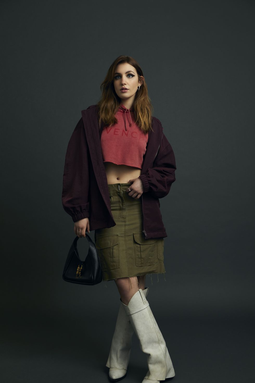 sophie nélisse wearing a cropped sweatshirt, green skirt, and white boots