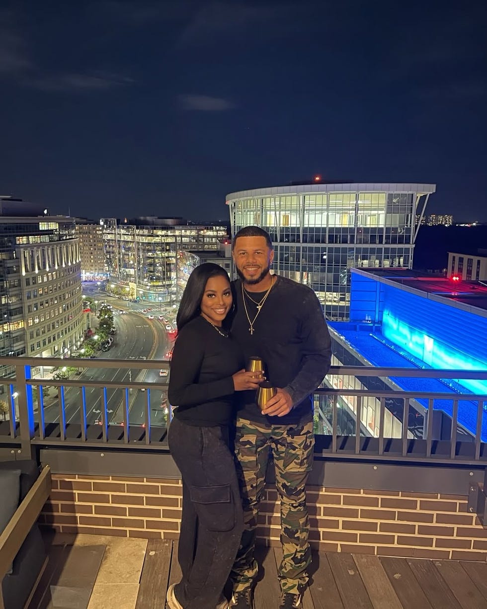 two individuals on a rooftop at night holding drinks with a city background