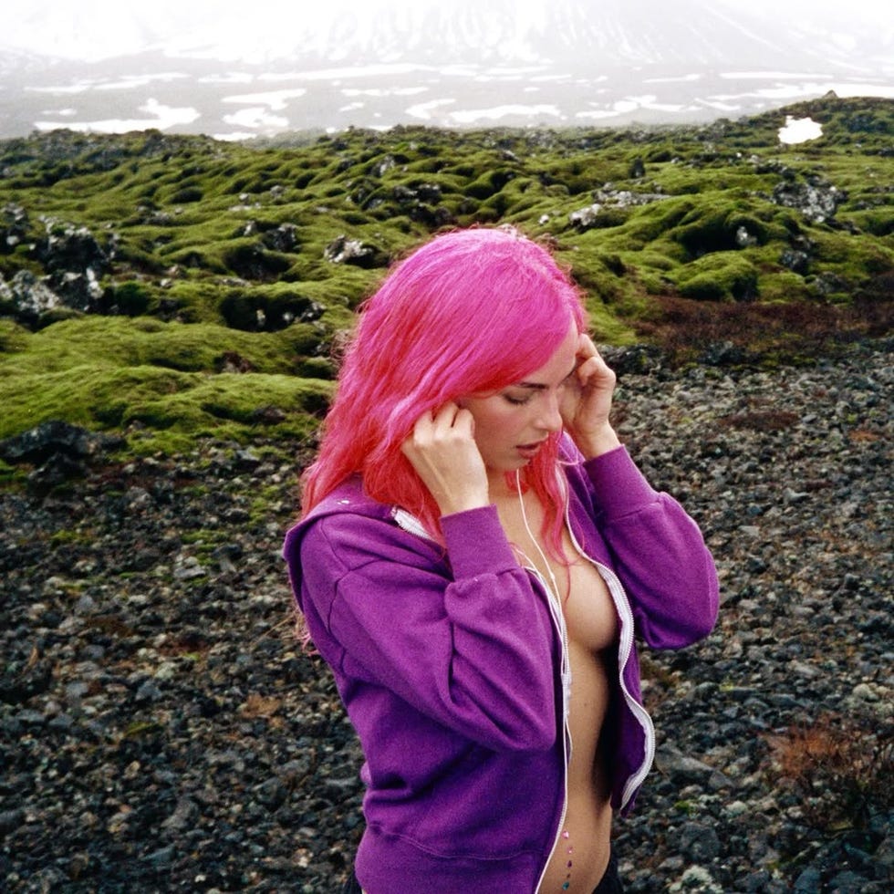 person with pink hair wearing a purple hoodie in a natural landscape