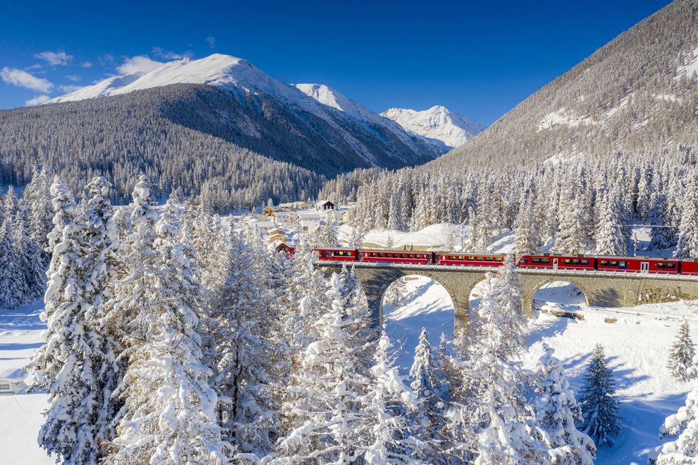 winter sun over bernina express train on viaduct in the snowy landscape, chapella, graubunden canton, engadine, switzerland