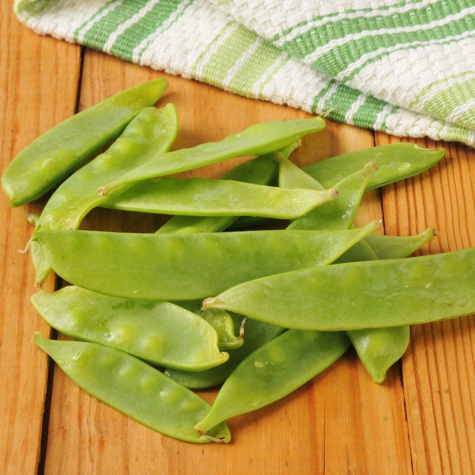 fresh washed snow peas on a rustic wooden table with a kitchen towel