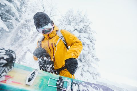 snowboarder in yellow jacket fixes his snowboard on a blustery day