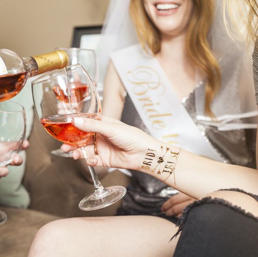 redhead woman wearing bride to be bachelorette party outfit with veil and sash drinking wine with friends
