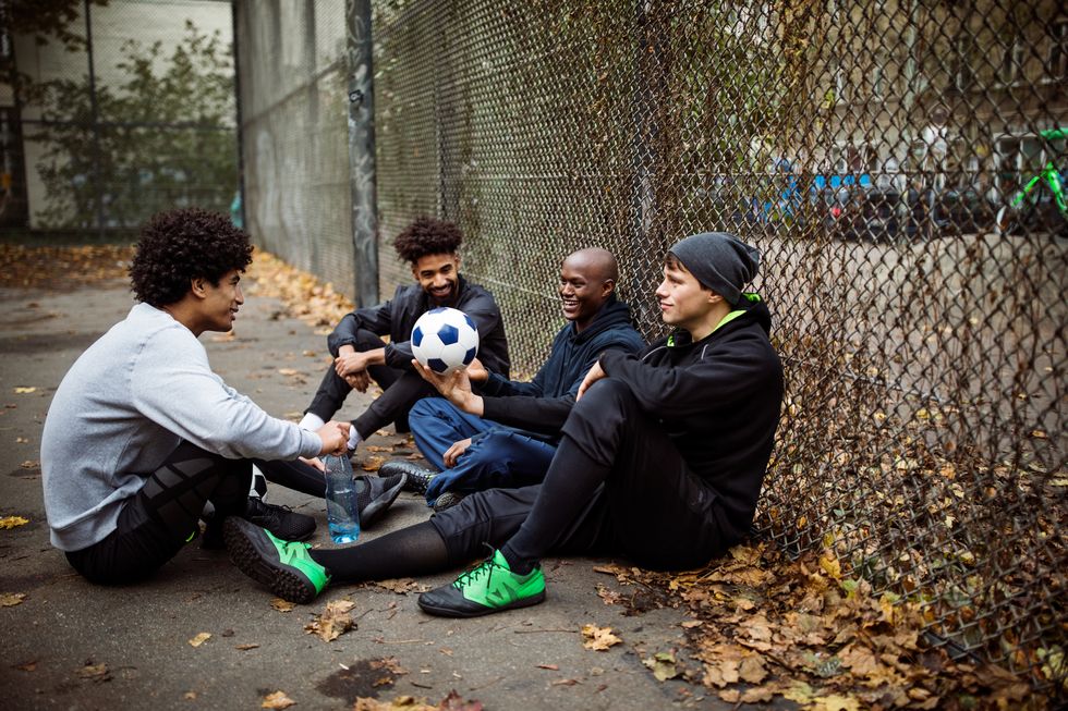 Soccer players talking while sitting against fence