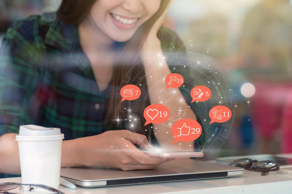 Social media concept, Asian woman hand using mobile phone to check social network application with number of Like, Love, comment, people and fovorite icon at desk beside glass in coffee shop