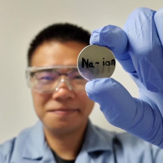 researcher junhua song, smiling, holding up a sodium ion disk