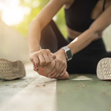 soft focus woman massaging her painful foot while exercising. running sport injury concept.