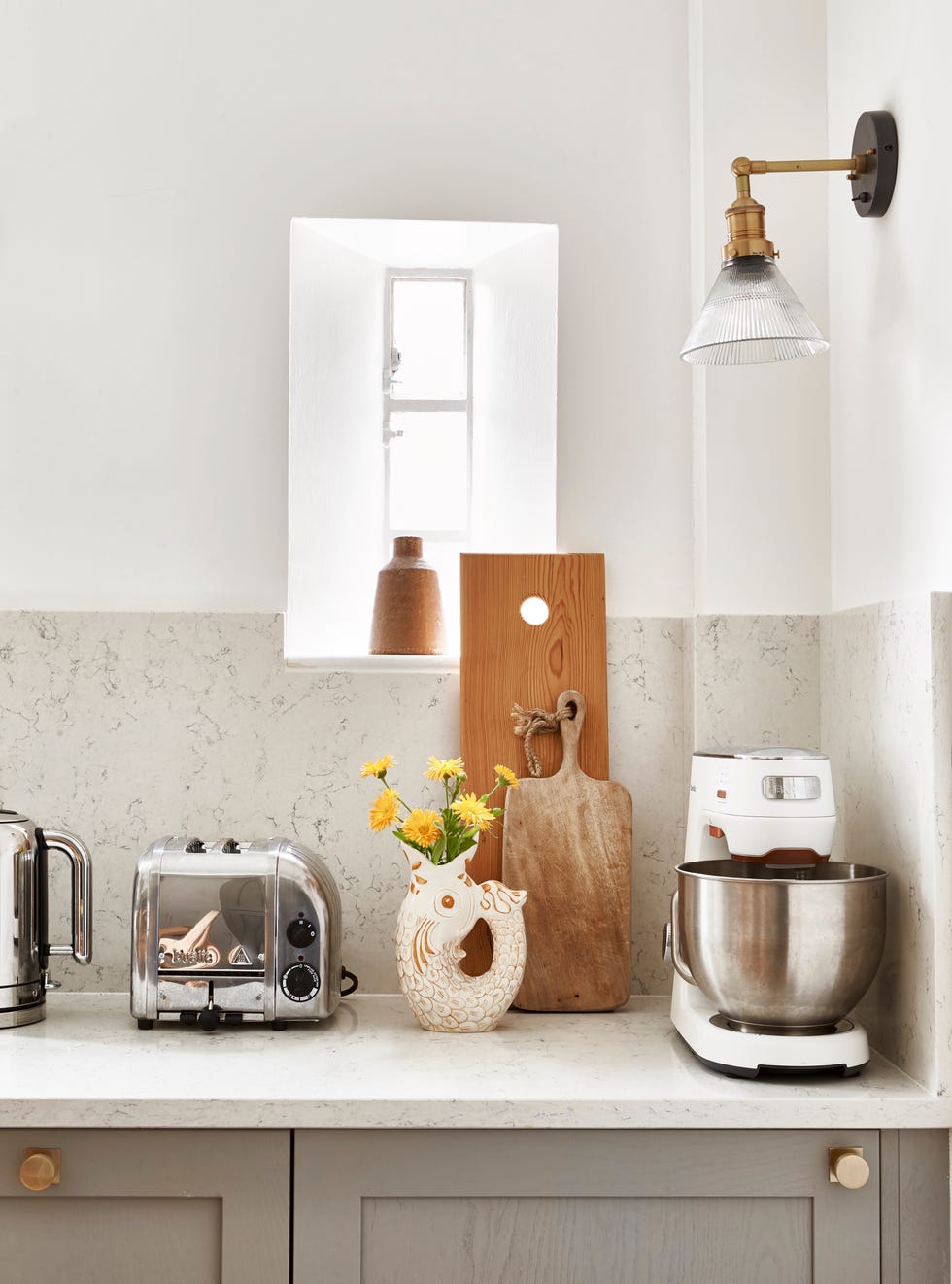 Soft grey kitchen cabinets, quartz worktops and splashback, appliances and a vase with fresh flowers