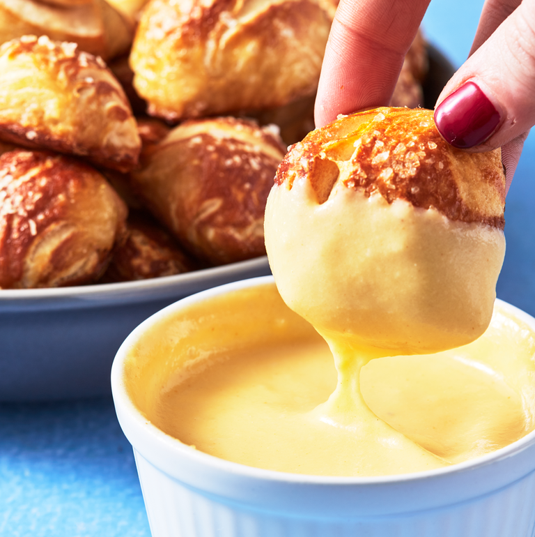 soft pretzel bite made of biscuit dough being dipped in cheese