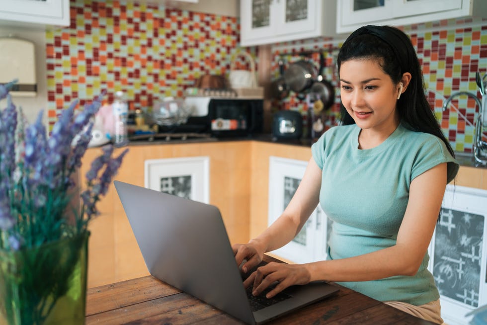 software developer asian woman having video conference with diverse people collage on laptop in the kitchen telework