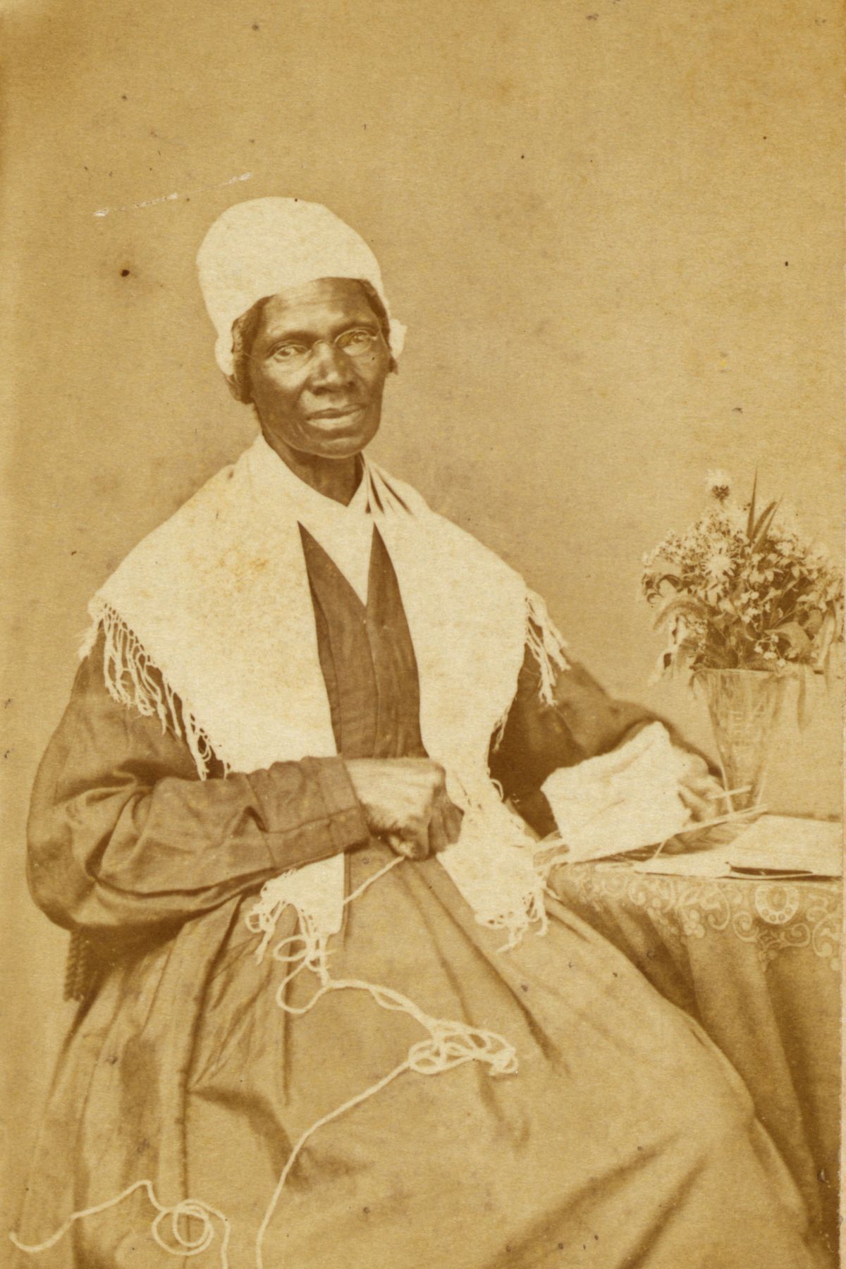 Sojourner Truth, three-quarter length portrait, seated at table with knitting and book
