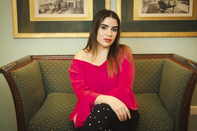 la periodista sentada en un sofa con jersey rosa