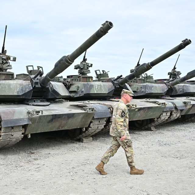 a line of m1 abrams tanks with an army soldier walking in front