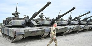 a line of m1 abrams tanks with an army soldier walking in front