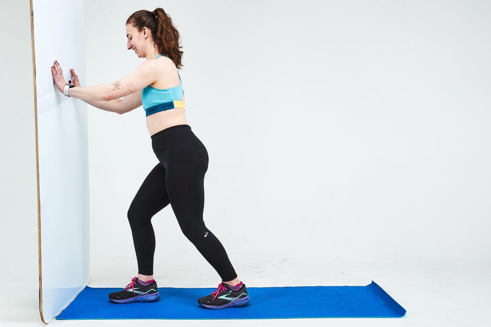 a woman performing a stretching exercise against a wall