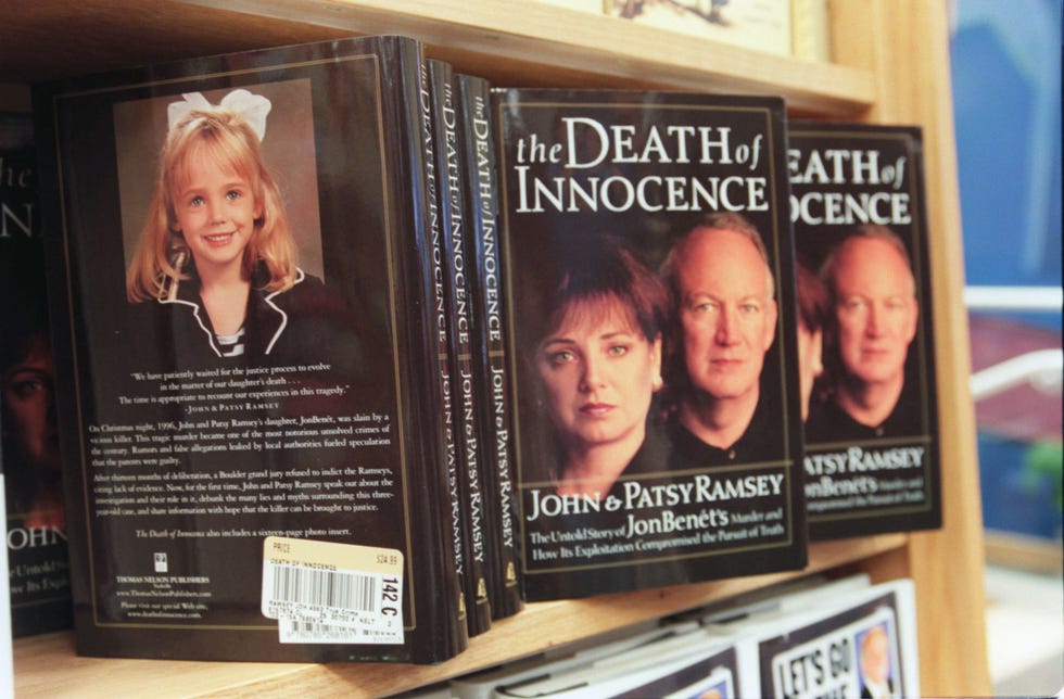several copies of a book titled the death of innocence rest on a wooden shelf