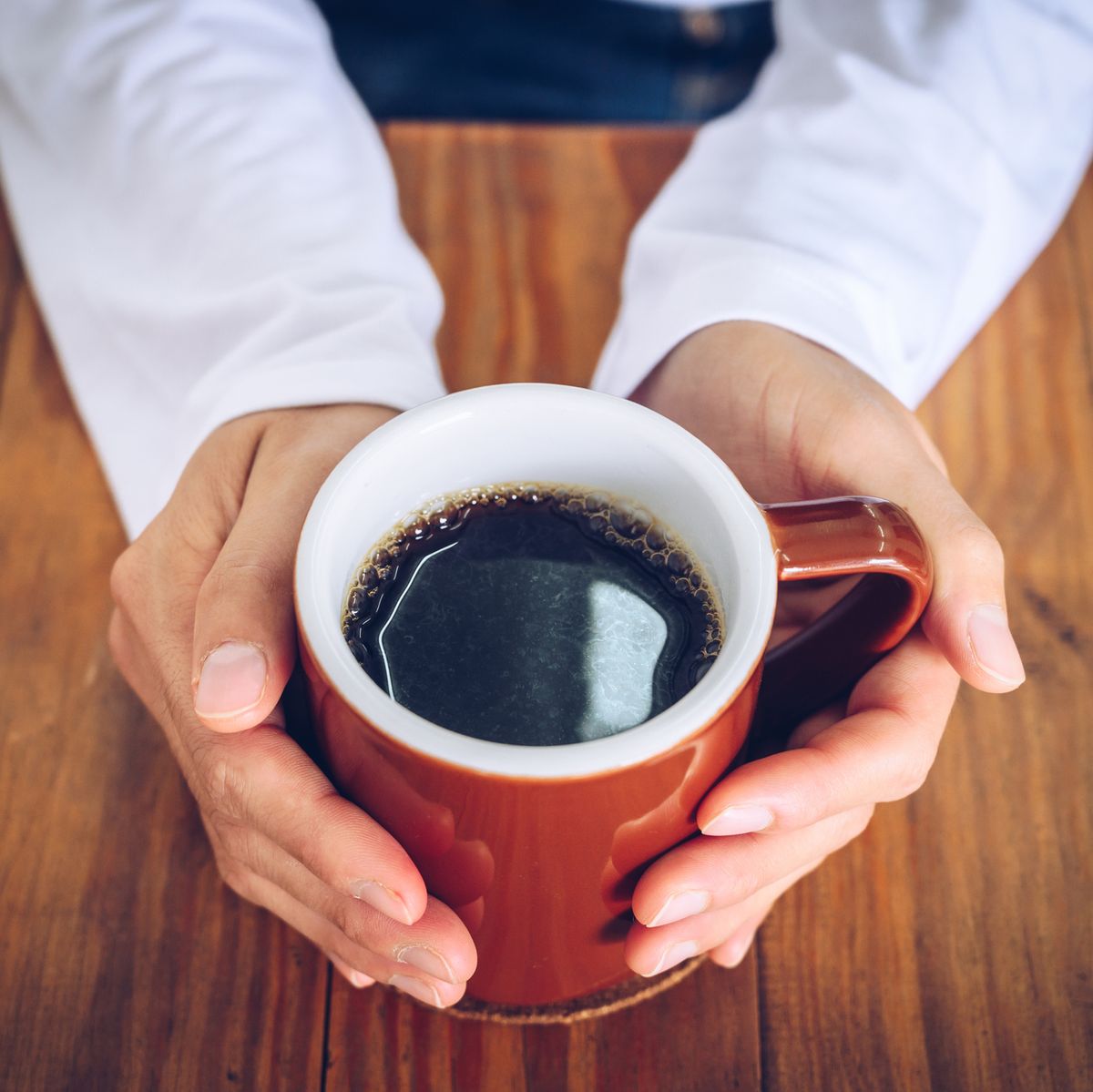 someone hands holding a mug of black coffee before drinking